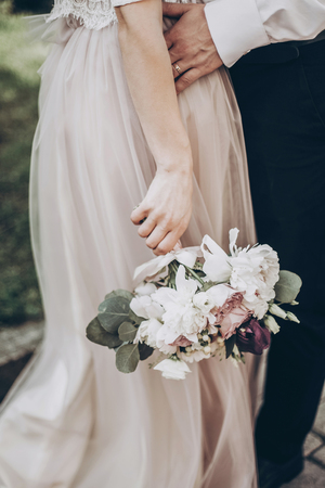 stylish wedding bouquet. modern bride and groom holding fashionable bouquet close up in park. fine art wedding photo, romantic momentの写真素材