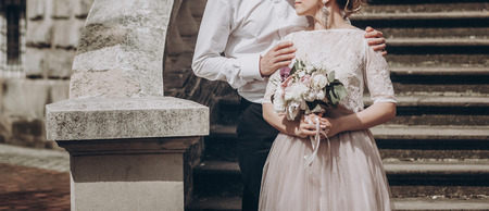 stylish wedding couple with bouquet. modern bride and groom holding fashionable bouquet at old stairs at castle. fine art wedding photo, romantic momentの写真素材