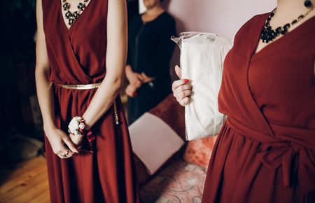 stylish bridesmaids with red and white flowers on boutonniere on hand and in red dress. beautiful woman helping bride in the morningの写真素材