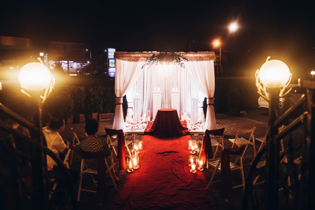 wedding evening ceremony, venue aisle with candles in glass lanterns and arch, stylish wedding decoration for night ceremony in garden, lights. beautiful romantic place for love celebrationの写真素材
