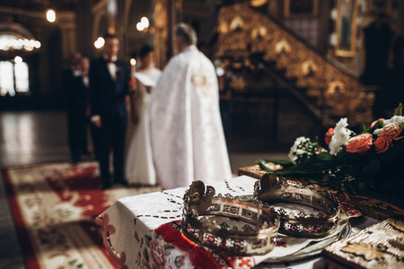 golden crowns on altar and priest putting on golden wedding rings on couple hand in church wedding ceremony, religion traditionsの写真素材