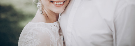 stylish wedding bride smiling. modern bride hugging groom, lips and earrings close up. fine art wedding photo, romantic moment, long edgeの写真素材
