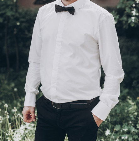 stylish groom in white shirt with black bow tie. wedding groom posing in sunny garden, fine art wedding photo, romantic momentの写真素材