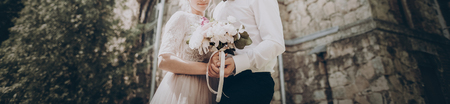 stylish wedding couple with bouquet. modern bride and groom holding fashionable bouquet  and posing at old castle. fine art wedding photo, romantic moment, long edgeの写真素材