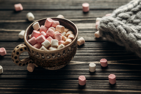 stylish rustic winter wallpaper of cup with colorful marshmallows and big yarn on wooden background with space for text. greeting card. cozy mood autumn. seasonal holidays conceptの写真素材