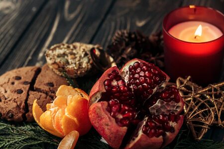 stylish rustic christmas wallpaper candle and presents with red ribbon and garnet cookies fruits on wooden background with green branches. seasonal greetings for winter holidays card conceptの写真素材