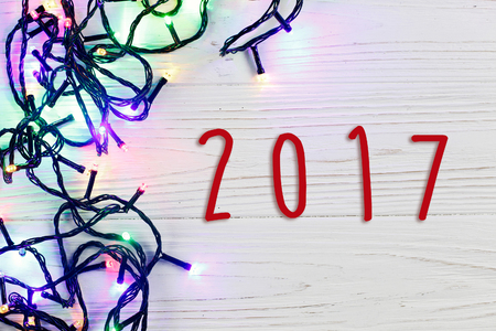 2017 sign text on christmas frame of garland lights. colorful stylish border on white rustic wooden...