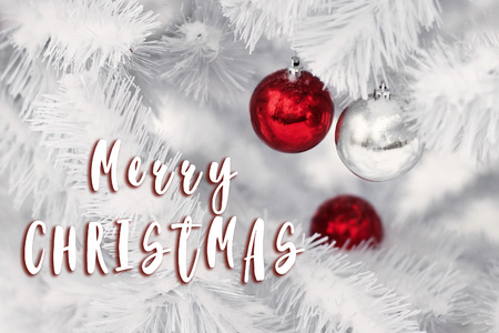 merry christmas text sign on stylish red and silver ornament balls on white christmas tree branches....