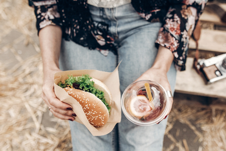 juicy burger and lemonade in hands, top view. stylish hipster woman holding  cheeseburger and refreshing drink. boho girl at street food festival. summer vacation picnic. space for textの写真素材