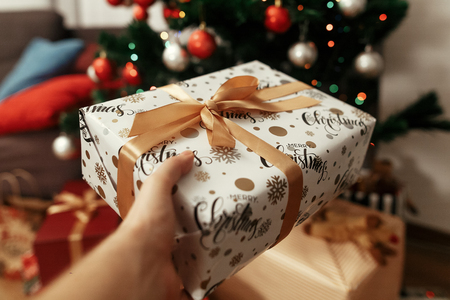 hand holding stylish christmas present on background of  tree and lights. giving box. gift ideas....