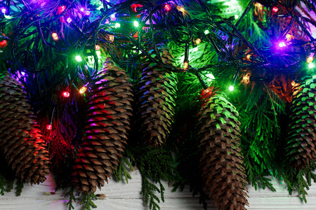 christmas garland lights and pine cones on fir branches. stylish white rustic wooden background....
