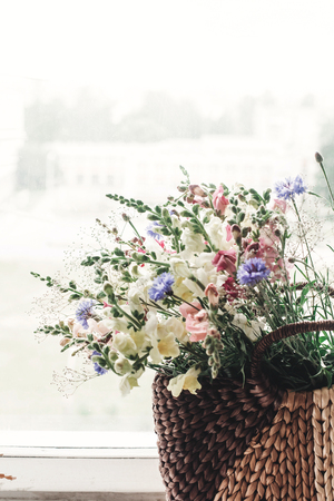 beautiful herbs wildflowers in wicker bag on rustic white window. colorful flowers in brown basket in sunlight, space for text. rural atmospheric moment. unusual summer pictureの写真素材