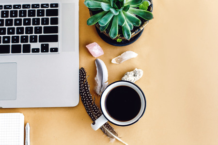stylish laptop phone and notebook and coffee with feathers crystals on craft background,  planning...