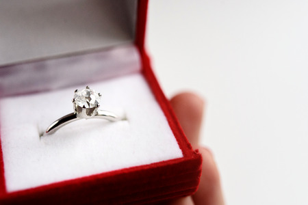 luxury ring with diamond in stylish red box in hand on white background, present and love concept,...