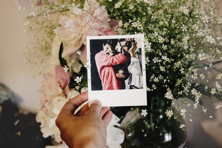 woman holding photo card with polaroid picture of her family on background of peoniesの写真素材