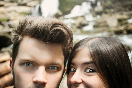 couple hipster travelers taking selfie and looking out with funny emotions at waterfall in...