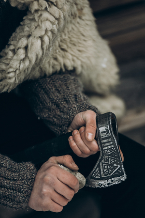 Northern warrior with weapon, viking sharpening his axe before battle hands close-up, scandinavian lumberjack with steel axe, viking costume cosplay, norway historical heritage conceptの写真素材