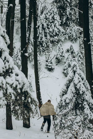 viking hunter in pelt walking in snow winter forest with steel axe and sword, viking warrior hunting in scandinavian woods before battle, thor cosplay outdoors, northern knight conceptの写真素材