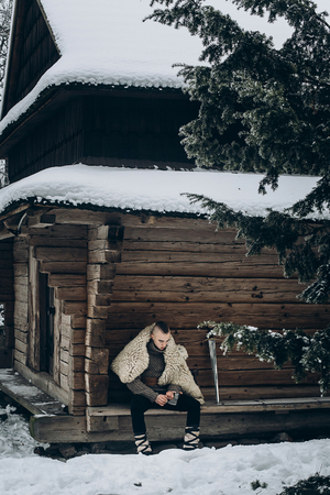 Brave viking warrior sharpening axe before battle in the north, scandinavian man with mohawk sitting near historical wooden building near sword, viking cosplay conceptの写真素材