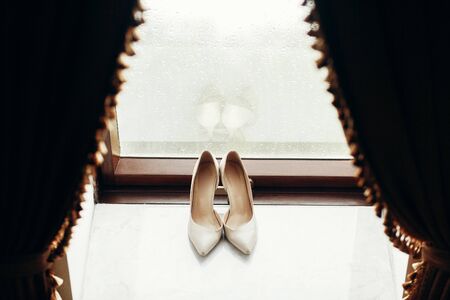 Elegant white shoes for bride on window sill, stylish leather wedding shoes, white high heel footwear, wedding clothing conceptの写真素材