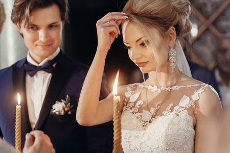 Beautiful bride and groom holding candles during wedding ceremony in church, gorgeous blonde bride and handsome groom performing spiritual ritual, marriage conceptの写真素材