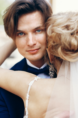 Happy newlywed groom hugging bride after wedding ceremony outdoors face close-up, newlywed couple portraitの写真素材