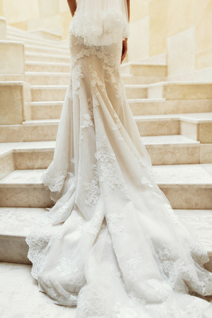Gorgeous bride in white long wedding dress posing on white marble stairs indoors before wedding ceremony, sexy bride standing on staircase dress closeupの写真素材