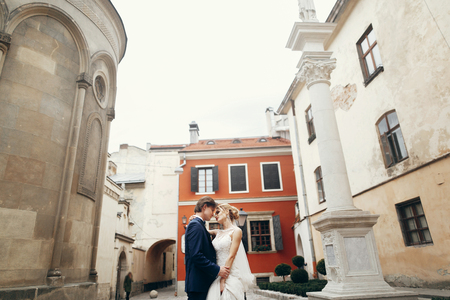 Romantic bride and groom hugging outdoors in old european street, newlywed bride in white wedding dress in sensual embrace with handsome groom, couple of dancers portraitの写真素材
