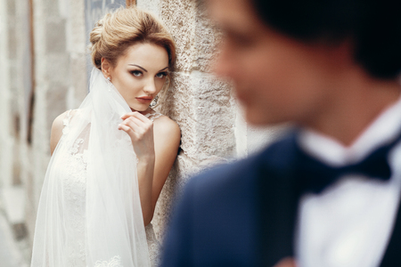 Gorgeous, sexy bride looking at happy handsome groom, newlywed couple portrait, beautiful bride face looking at stylish groom in suit, emotional wedding momentの写真素材