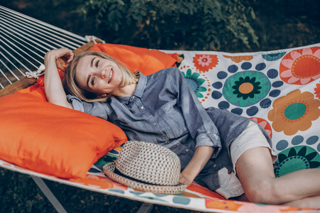 Smiling blonde hipster relaxing on a hammock in a park, summer leisure with woman lying outdoors, camping conceptの写真素材