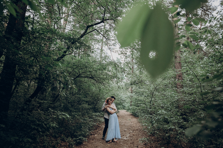 stylish hipster bride and groom walking and dancing in green summer forest. happy couple in love, modern outfit, relaxing at park. girl in dress and straw hat with peony. rustic wedding conceptの写真素材