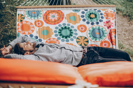 Handsome man relaxing on a hammock on a camping trip, stylish hipster man lying on a hammock thinking and looking at the sky near a lake, relaxation conceptの写真素材