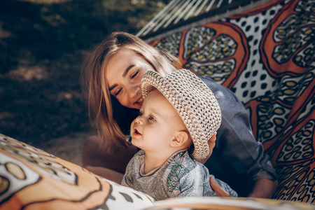 Family portrait, cute baby boy with young hipster mother relaxing and playing on a hammock while on vacation camping trip in a park, emotional face close-upの写真素材