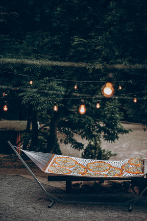Stylish hipster hammock under romantic lights in park at resort, family camping trip conceptの写真素材