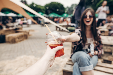 lemonade in hand. man giving lemonade to stylish hipster woman in sunglasses with red lips. cool boho girl with cocktail at street food festival. summer vacation, space for textの写真素材