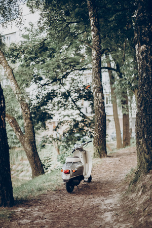 motorbike standing at road in green park. moped parked in forest, hipster transportation, summer vacation, space for textの写真素材
