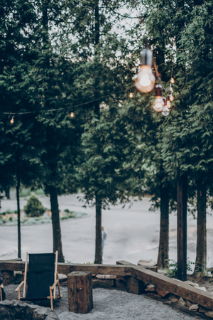 stylish wooden chair under retro lights in summer forest park. resting, camping and relaxing outdoor, summer vacation and holiday. space for text. wanderlust and adventure.の写真素材