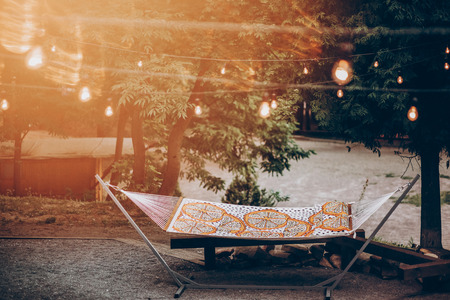 stylish travel hammock under retro lights in summer forest park. resting, camping and relaxing outdoor, summer vacation and holiday. space for text. wanderlust and adventure.の写真素材