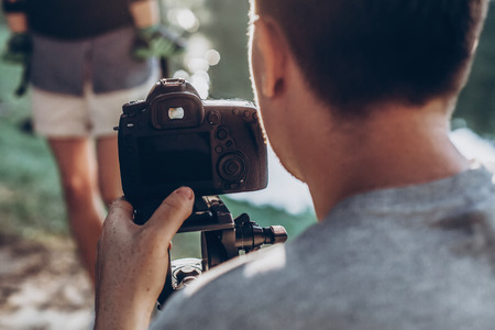 man holding photo camera and filming footage. Video camera operator working with his equipment in sunny summer parkの写真素材