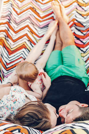 happy stylish family playing with cute daughter and cuddling, relaxing in hammock on summer vacation in evening sun light on the beach. hipster couple kissing and resting in sunset. space for textの写真素材