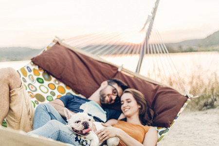 Hipster couple on a trip to the beach, young freelancer man relaxing in a hammock with his woman, romantic couple on vacation with bulldog petの写真素材