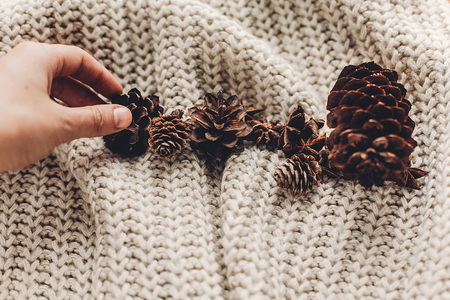 hand holding pine cone on background of cozy sweater with anise on rustic background, space for text. xmas seasonal greetings card. winter holidays mood. christmas decor preparationの写真素材
