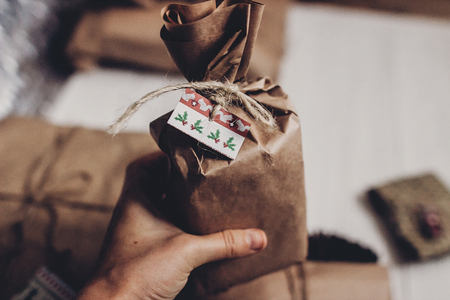 hand holding christmas presents. rustic craft present on white wooden background. stylish simple gifts wrapped in brown paper for christmas holidays. eco design. xmas seasonal greetingsの写真素材