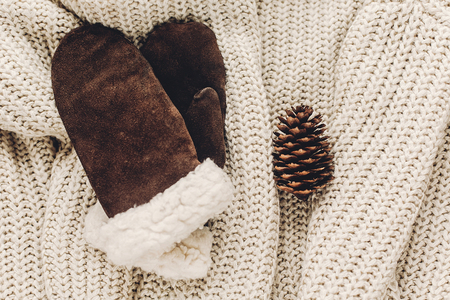 warm cozy gloves and pine cones on cozy sweater on rustic background top view, space for text. xmas seasonal greetings card. winter holidays mood. christmas flat layの写真素材