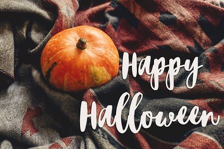 happy halloween text sign on autumn pumpkin on stylish scarf fabric, space for text. seasonal greetings, fall holidays. harvest time. cozy moodの写真素材