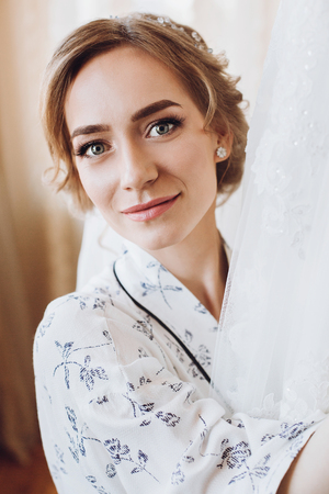 beautiful happy bride smiling, standing in silk robe at her luxury wedding dress. happy moments. marriage concept. bride getting ready in the morningの写真素材
