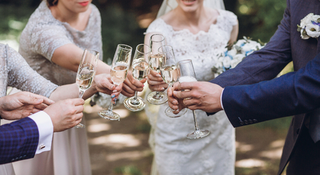 happy group of people toasting with champagne. hands holding glasses of champagne and clinking. bride bridesmaids and groom groomsmen having fun. holiday celebration. christmas feastの写真素材