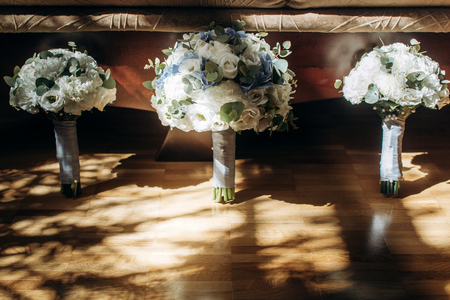 Beautiful white and blue roses wedding bouquets for bride and bridesmaids closeup, fresh white flowers bouquet on wooden background in roomの写真素材