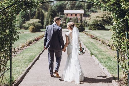 beautiful gorgeous bride and groom posing in sunny spring park among green leaves. happy wedding couple walking in green garden. happy marriage moments. elopement conceptの写真素材
