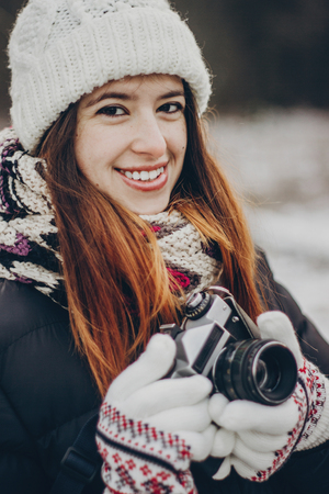 stylish hipster traveler girl with old photo camera exploring in snowy woods in winter. happy woman walking in cold forest. space for text. atmospheric moment. wanderlustの写真素材